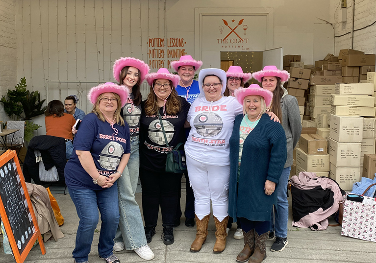 Hen party group outside The Craft Pottery wearing pink fluffy cowboy hats and Bride wearing white fluffy cowboy hat